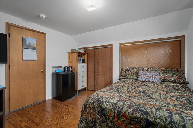 bedroom with multiple closets, vaulted ceiling, dark hardwood / wood-style flooring, and black refrigerator