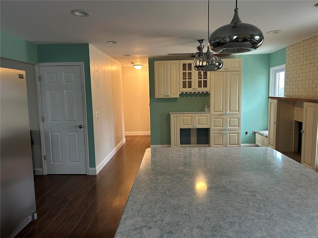 kitchen featuring dark wood finished floors, cream cabinets, glass insert cabinets, freestanding refrigerator, and a brick fireplace