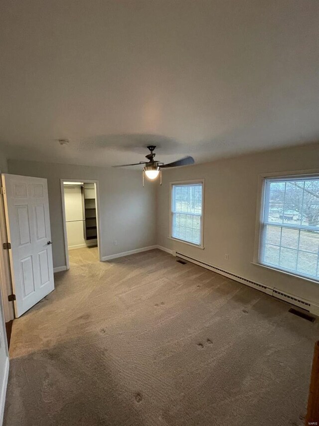 unfurnished bedroom with a baseboard heating unit, carpet flooring, a ceiling fan, baseboards, and a walk in closet