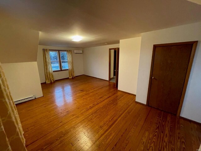 empty room with an AC wall unit, a baseboard radiator, and wood finished floors