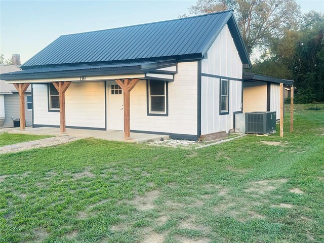 rear view of house featuring central air condition unit, a yard, and metal roof
