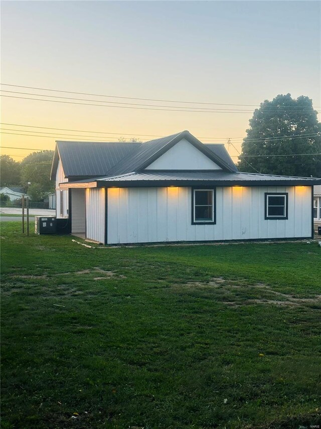 property exterior at dusk with board and batten siding, a yard, and metal roof