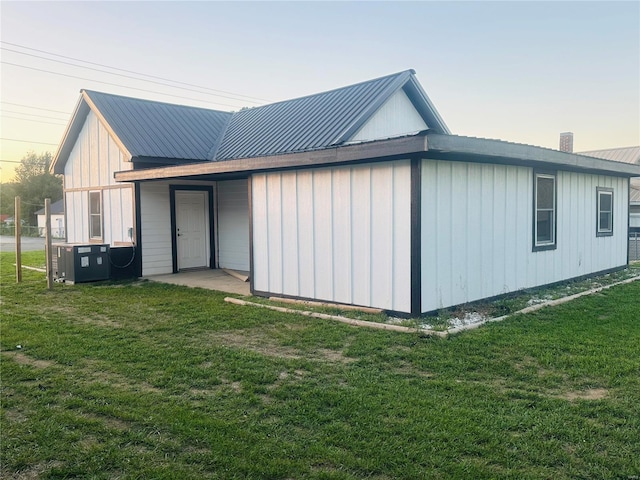 exterior space featuring board and batten siding, metal roof, a lawn, and central air condition unit