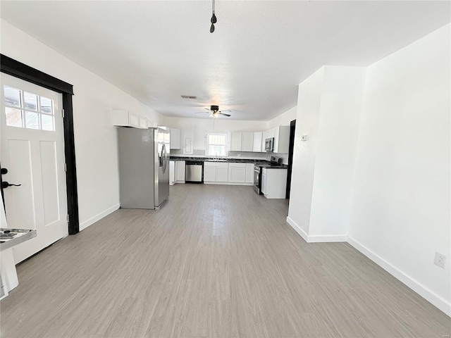unfurnished living room with light wood-style floors, a ceiling fan, visible vents, a sink, and baseboards