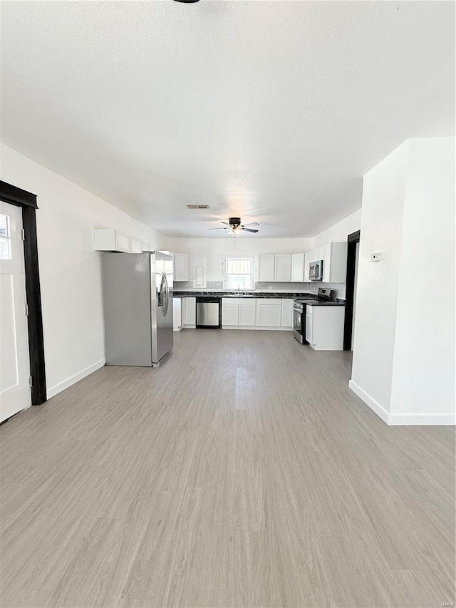 unfurnished living room with light wood-style flooring, a textured ceiling, baseboards, and a ceiling fan