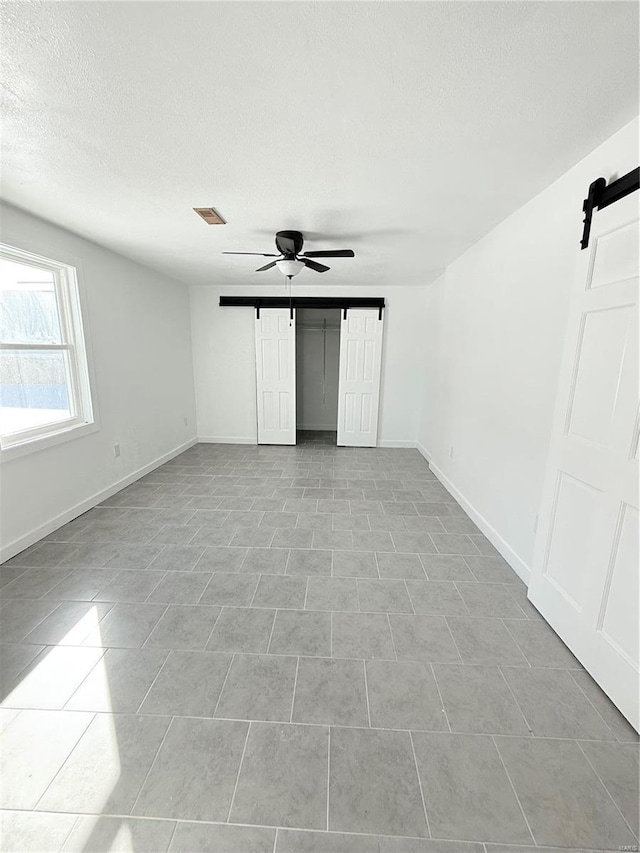 unfurnished bedroom with a textured ceiling, baseboards, visible vents, and a barn door