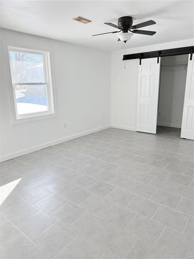 unfurnished bedroom with a closet, a ceiling fan, visible vents, a barn door, and baseboards