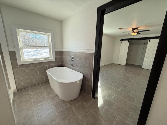 full bath with a ceiling fan, tile patterned flooring, wainscoting, tile walls, and a freestanding bath