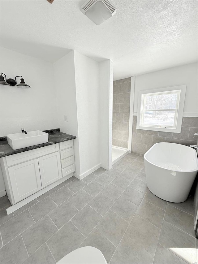 full bath with a tile shower, a soaking tub, a textured ceiling, vanity, and visible vents
