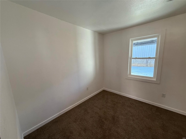 unfurnished room featuring baseboards and dark carpet