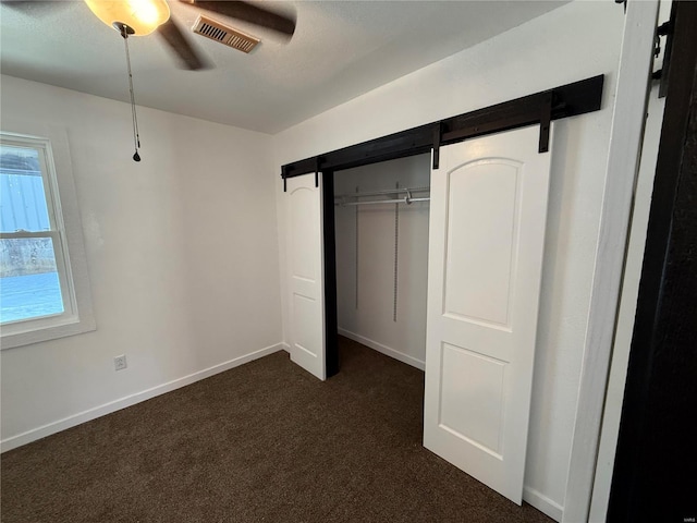 unfurnished bedroom with a closet, a ceiling fan, visible vents, dark colored carpet, and baseboards