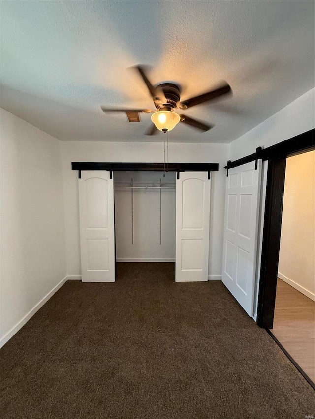 unfurnished bedroom featuring dark colored carpet, a barn door, a textured ceiling, and baseboards