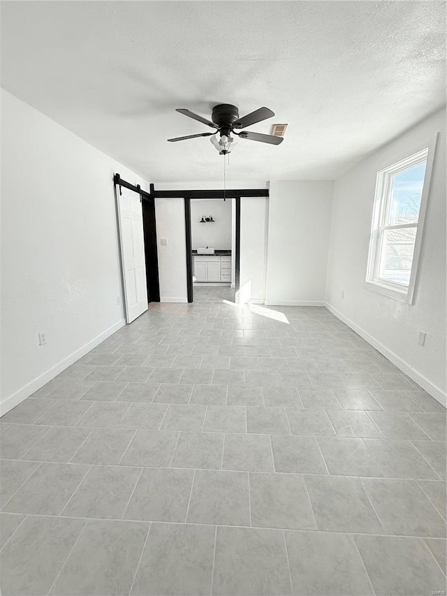 spare room featuring baseboards, a textured ceiling, a barn door, visible vents, and ceiling fan