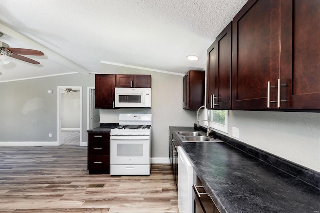kitchen with dark countertops, a sink, white appliances, light wood-style flooring, and a ceiling fan