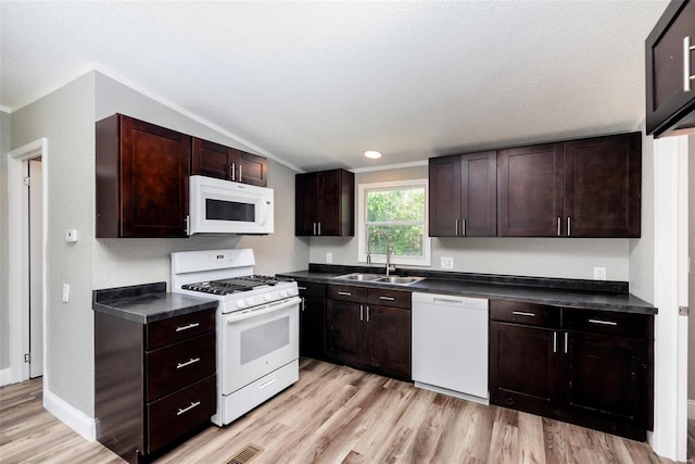 kitchen featuring dark brown cabinets, dark countertops, a sink, light wood finished floors, and white appliances