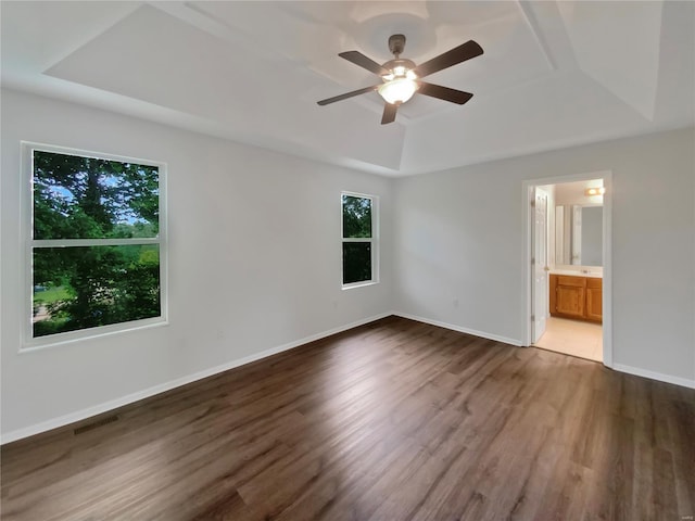 unfurnished bedroom with connected bathroom, ceiling fan, a raised ceiling, and dark hardwood / wood-style flooring