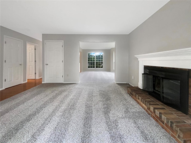 unfurnished living room featuring dark carpet and a brick fireplace