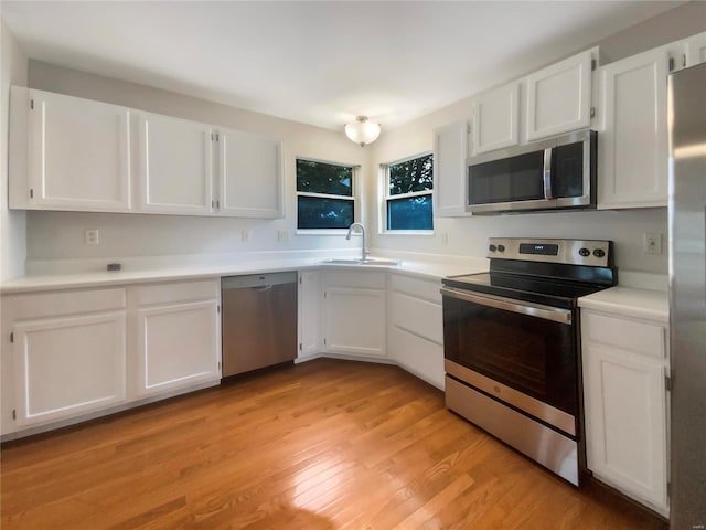 kitchen with appliances with stainless steel finishes, white cabinetry, sink, and light hardwood / wood-style flooring