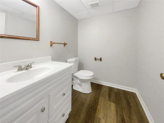 bathroom with wood-type flooring, vanity, toilet, and a paneled ceiling