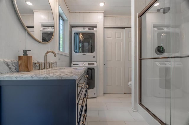 bathroom with a shower with shower door, vanity, stacked washer / drying machine, toilet, and tile patterned floors