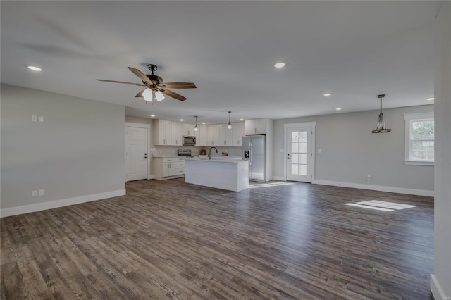 unfurnished living room with ceiling fan, sink, dark wood-type flooring, and a wealth of natural light