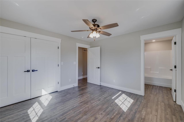 unfurnished bedroom featuring hardwood / wood-style floors, ensuite bath, ceiling fan, and a closet