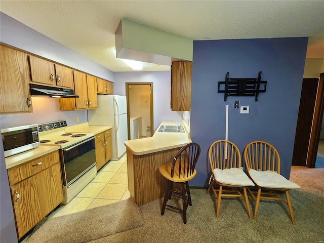 kitchen featuring sink, a breakfast bar area, kitchen peninsula, light colored carpet, and white appliances