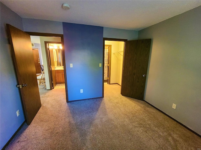 unfurnished bedroom with a spacious closet, a closet, light carpet, and a textured ceiling