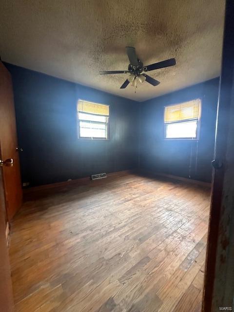 unfurnished room with ceiling fan, hardwood / wood-style flooring, a textured ceiling, and a wealth of natural light