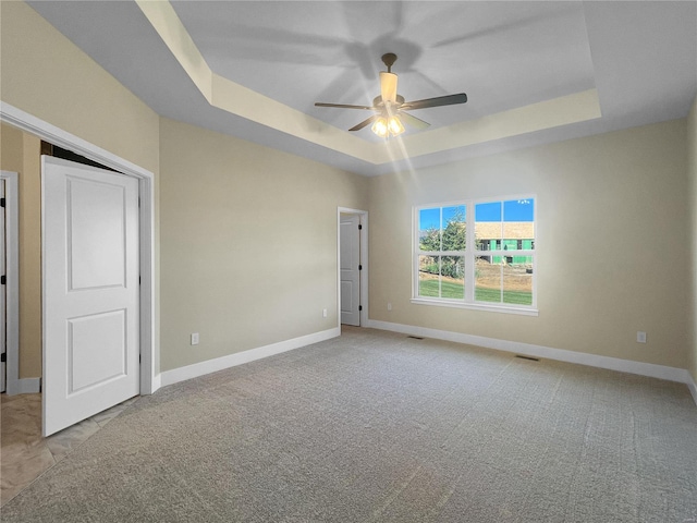 carpeted spare room with a tray ceiling and ceiling fan