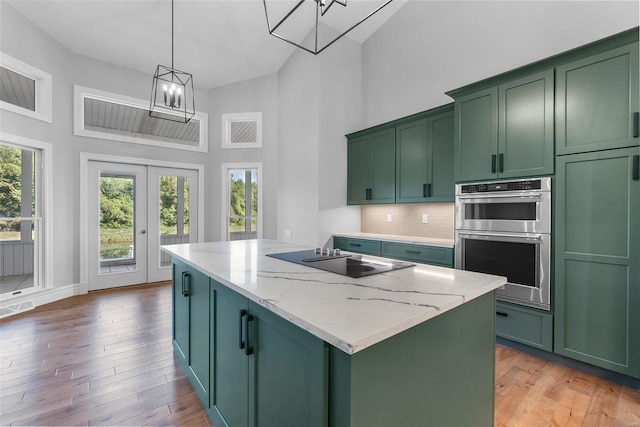 kitchen with light stone counters, black electric cooktop, green cabinetry, and decorative light fixtures