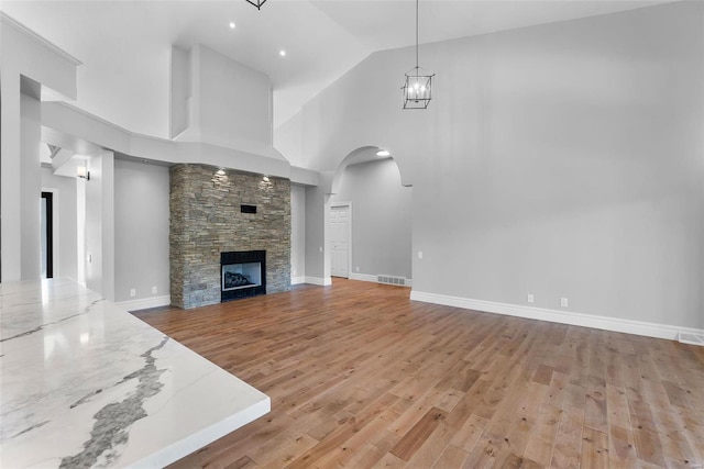 unfurnished living room featuring a fireplace, high vaulted ceiling, an inviting chandelier, and light wood-type flooring