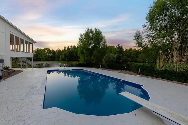 pool at dusk featuring a diving board, a sunroom, and a patio