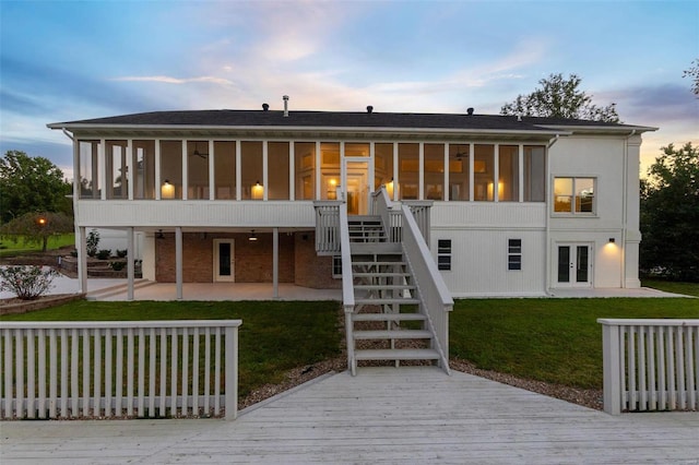 back house at dusk featuring a sunroom, a lawn, and a patio area