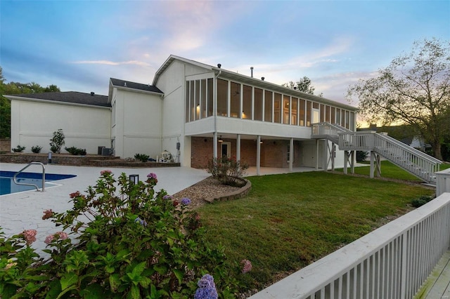 back house at dusk featuring a pool side deck, a sunroom, a yard, and a patio area