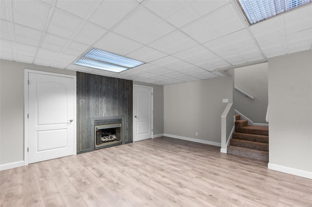 unfurnished living room with a large fireplace, wood walls, a drop ceiling, and light hardwood / wood-style flooring