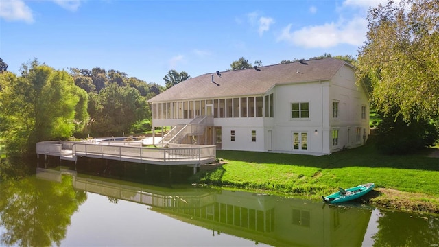 rear view of house with a yard, a sunroom, and a deck with water view