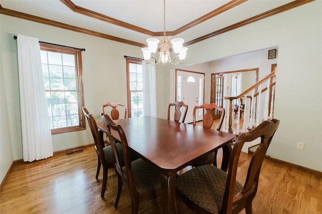 dining space featuring light hardwood / wood-style flooring, a chandelier, ornamental molding, and a tray ceiling