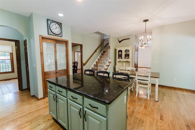 kitchen with dark stone counters, a kitchen island, light hardwood / wood-style flooring, decorative light fixtures, and green cabinetry