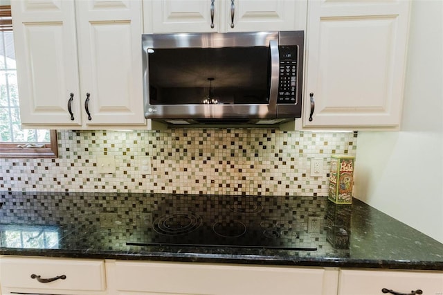 kitchen with decorative backsplash, dark stone countertops, black stovetop, and white cabinetry