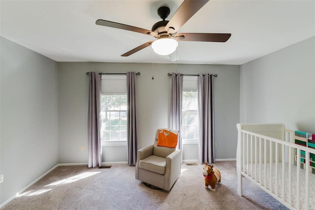 bedroom featuring light carpet, a nursery area, and ceiling fan