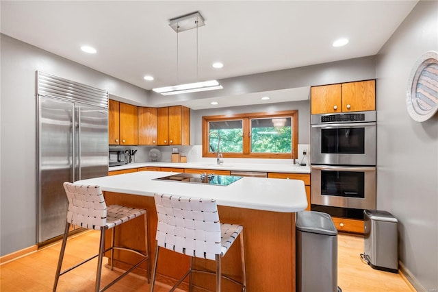 kitchen with a kitchen island, black appliances, light hardwood / wood-style floors, decorative light fixtures, and a kitchen breakfast bar