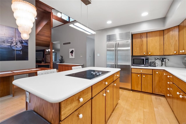 kitchen with a kitchen island, light wood-type flooring, stainless steel appliances, pendant lighting, and an inviting chandelier