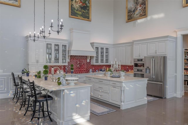 kitchen with appliances with stainless steel finishes, a center island with sink, premium range hood, and white cabinets