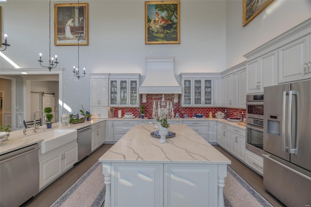 kitchen featuring appliances with stainless steel finishes, hanging light fixtures, custom range hood, and white cabinetry