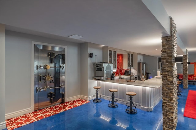 interior space featuring concrete flooring, stainless steel refrigerator, and ornate columns