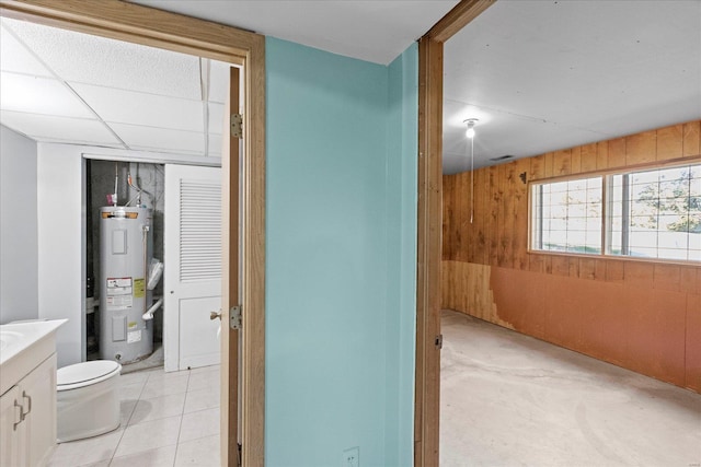 bathroom with water heater, vanity, wood walls, tile patterned flooring, and toilet