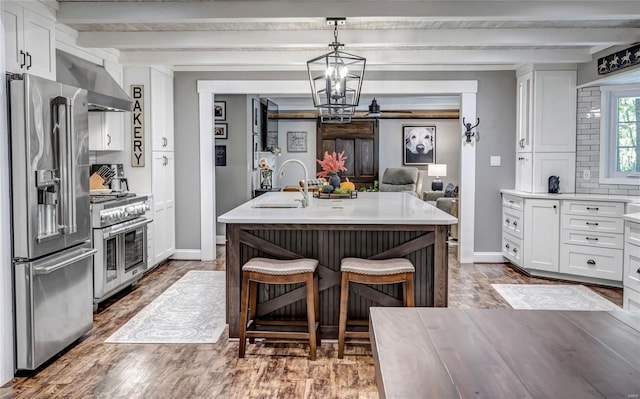 kitchen with white cabinets, premium appliances, wall chimney exhaust hood, light countertops, and a sink