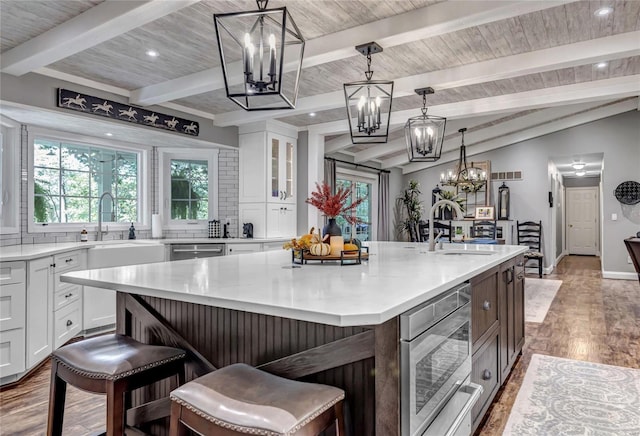 kitchen featuring glass insert cabinets, a center island with sink, white cabinetry, and light countertops