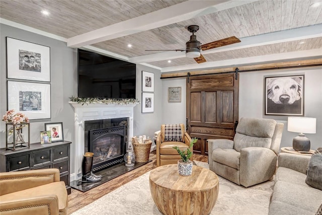 sitting room featuring a barn door, light wood-style floors, a glass covered fireplace, a ceiling fan, and beamed ceiling